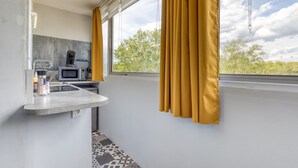 Moderni keittiö, jossa on mikroaaltouuni, vedenkeitin ja kahvinkeitin, pieni pesuallas sekä ikkuna, jossa on verhot.