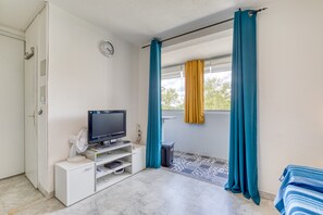 Une pièce équipée d’un téléviseur, d’une petite armoire, d’un ventilateur et d’une fenêtre avec des rideaux.