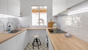 A modern kitchen with white cabinets, a wooden countertop, a sink, a stool, a toaster, and a window with a view of a balcony.