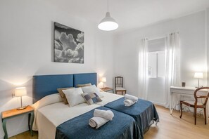 A bedroom with a bed, two bedside tables, a desk, a chair, a hanging light, and a wall-mounted picture.