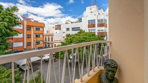 A balcony with a railing, overlooking a street with buildings and greenery.