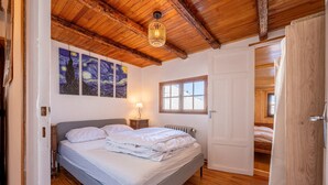 A bedroom with a wooden ceiling, a bed, a nightstand, a lamp, a window, and a door. - Apartment 'Grand Balcon' with Mountain View and Balcony (Albiez-Montrond)