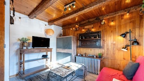 A cozy room with a wooden ceiling, a television, a red sofa, and a table with a lamp. - Apartment 'Grand Balcon' with Mountain View and Balcony (Albiez-Montrond)