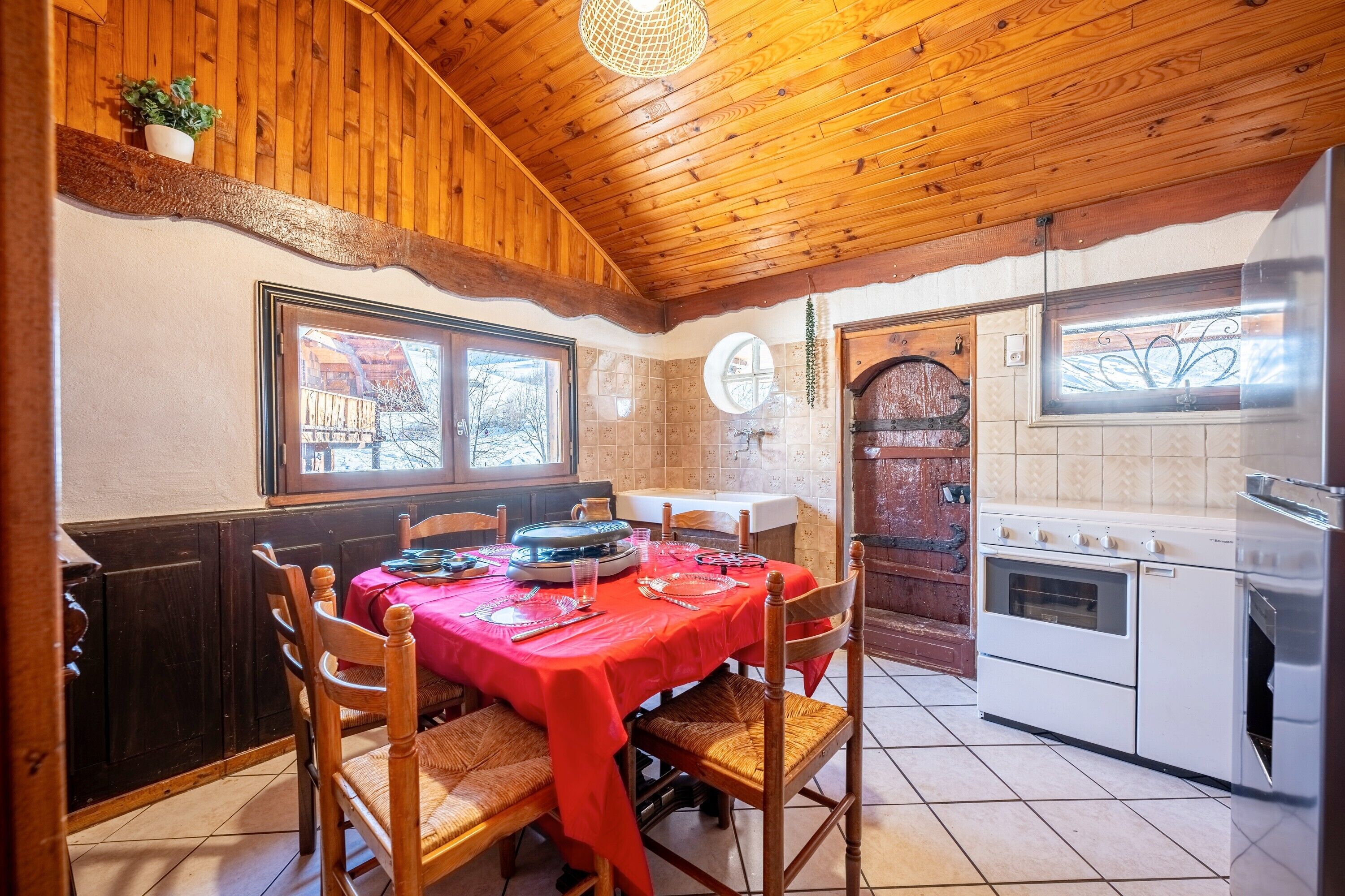 A wooden interior with a dining table set for four, a kitchen with a stove, and a window with a view.