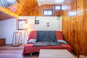 Ein gemütlicher Raum mit Holzwänden, einem roten Sofa, einem kleinen Tisch und einer Stehleiter.