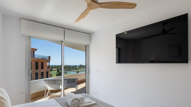 Ein modernes Hotelzimmer mit einem großen Bett, einem Deckenventilator, einem an der Wand montierten Fernseher und einem Balkon mit Blick auf die Stadt.