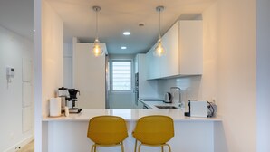 Eine moderne Küche mit weißen Schränken, einer Kaffeemaschine und zwei gelben Stühlen an der Arbeitsplatte.
