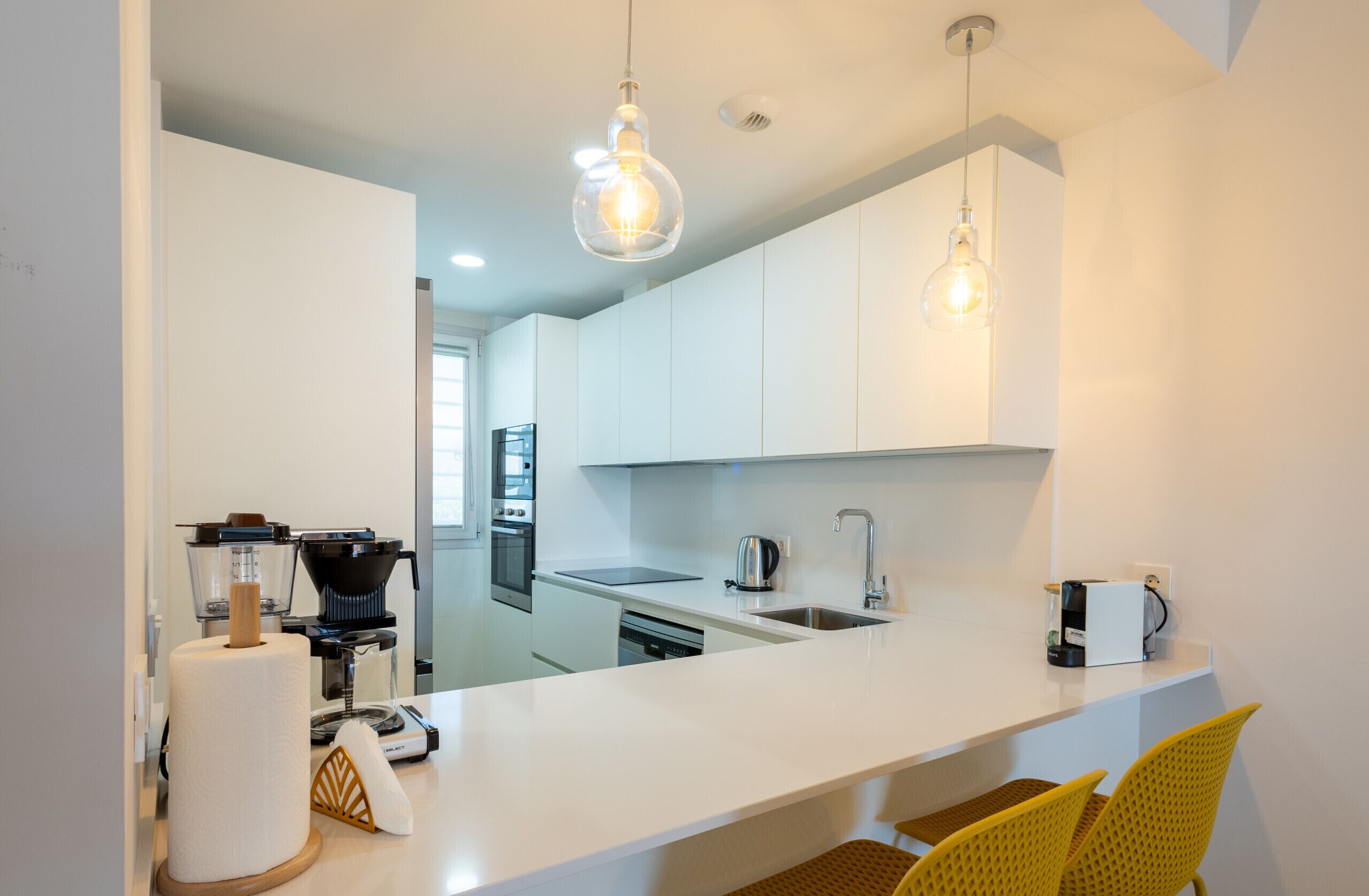 A modern kitchen with white cabinets, a white countertop, a coffee machine, and a sink.