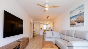 Ein modernes Wohnzimmer mit Flachbildfernseher, Couchtisch aus Holz, grauem Sofa und Deckenventilator.