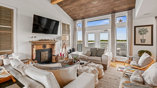 A spacious living room with a fireplace, comfortable seating, and large windows offering a view of the outdoors.