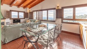 Un vaste espace de vie comprenant une table à manger avec un plateau en verre, des sièges confortables, un canapé et un téléviseur.