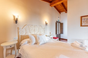 A bedroom with a white bed, two bedside tables, a nightstand, a mirror, and a door.