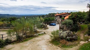 Un bâtiment rustique en pierre, avec un toit rouge, entouré de verdure et accessible par un chemin de terre.