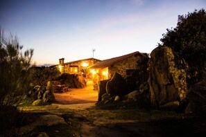 Um edifício de pedra com uma rocha grande em frente, um banco de madeira e céu claro.