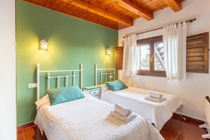A bedroom with two beds, a wooden ceiling, and a window with curtains.