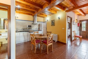 A kitchen with wooden beams, a dining table with chairs, a microwave, and a refrigerator.