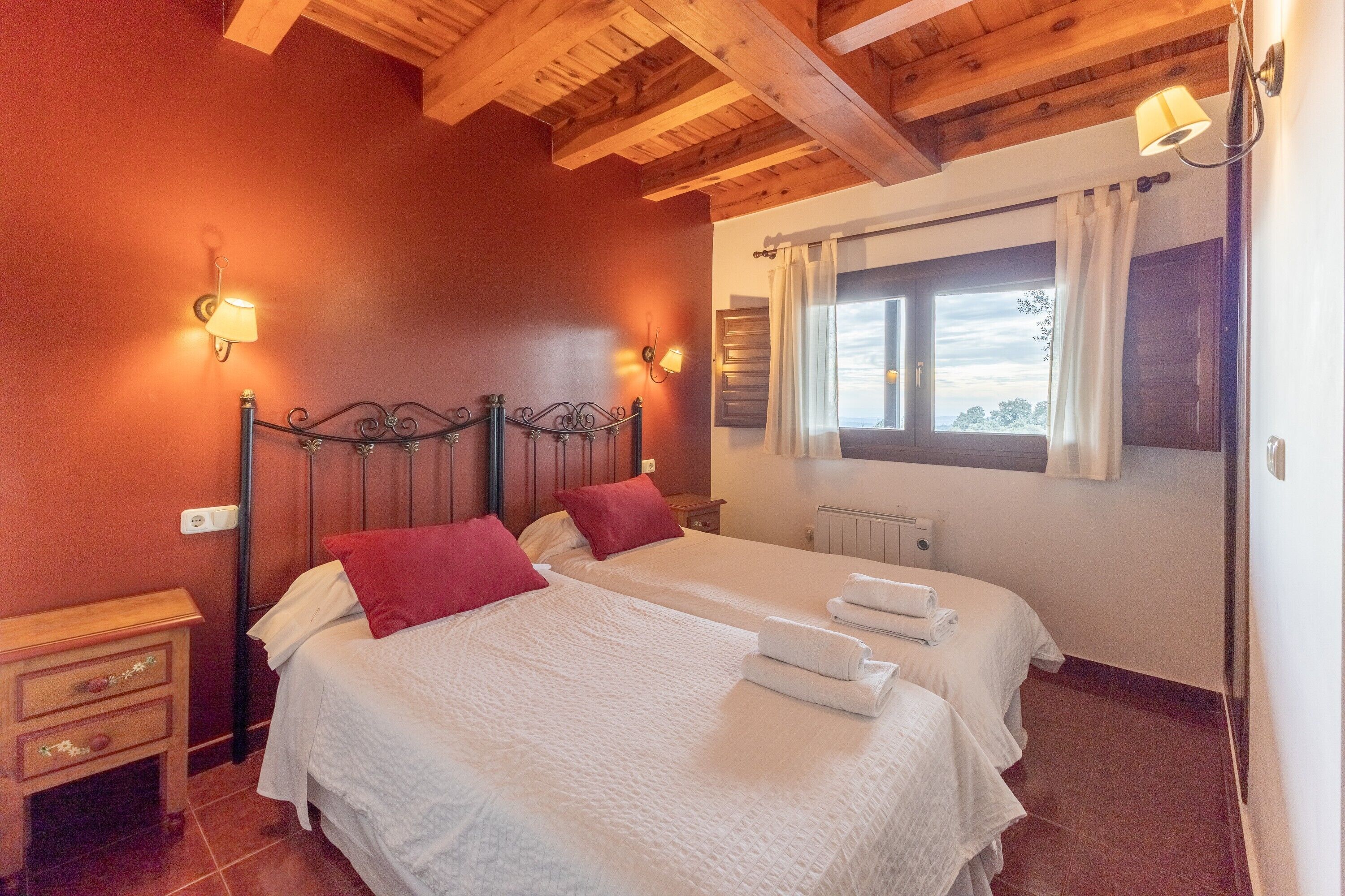 Un dormitorio con dos camas, vigas de madera en el techo, una ventana con cortinas y lámparas fijadas a la pared.