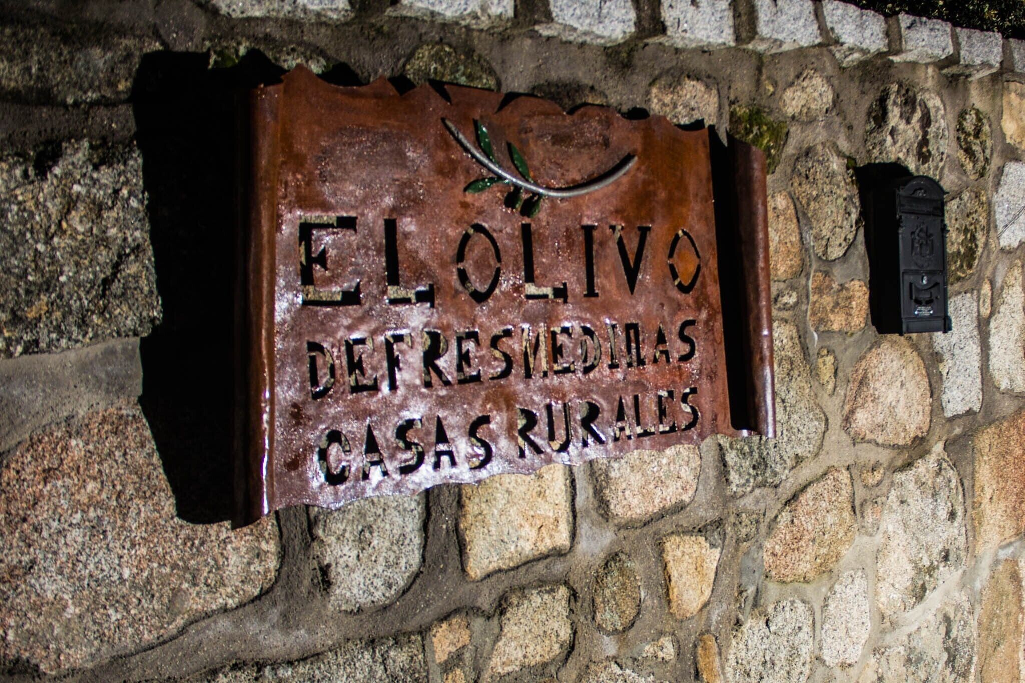 A sign with the text 'EL OLIVO REFRESSED CASAS RURALES' mounted on a stone wall.
