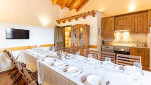 Un comedor con una mesa larga dispuesta para una comida, sillas de madera, techo de madera y una cocina con armarios y electrodomésticos de madera.