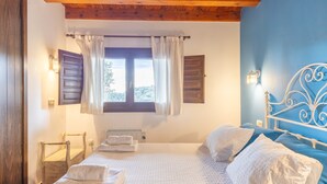 Un dormitorio con cama, ventana con cortinas, cabecero y lámpara fijada a la pared.