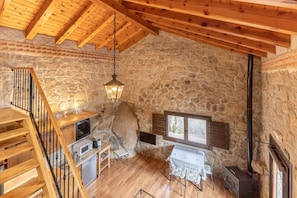 A rustic stone interior with a wooden staircase, a dining area, and a fireplace.