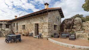 A stone building with a tiled patio, outdoor seating, and a view of the surrounding landscape. - Apartment 'Casa De Piedra' with Shared Pool, Private Terrace and Wi-Fi (Fresnedillas de la Oliva)