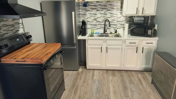 A kitchen with a stainless steel refrigerator, a built-in oven, a microwave, and a sink with a modern faucet. - Serenity's Sanctuary in this quiet, peaceful 2 bdr 1 bath bungalow. Pet friendly (Cushing)