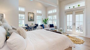 A spacious bedroom with a large bed, a seating area with a sofa and chairs, and a view of the outdoors through large windows. - Resort Style Pools, Sleeps 2,  Golf Cart Boardwalk to the Beach (Port Aransas)
