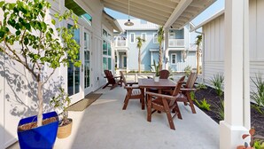 An outdoor patio with a wooden table and chairs, surrounded by potted plants and a view of neighboring houses. - Resort Style Pools, Sleeps 2,  Golf Cart Boardwalk to the Beach (Port Aransas)