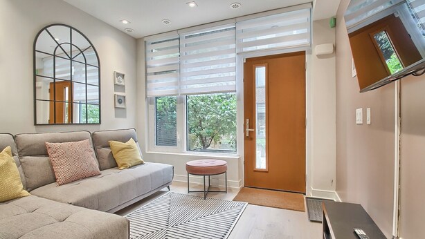A modern living room with a sofa, ottoman, and a large window with blinds. - Luxury Townhouse in Downtown Toronto (Toronto)