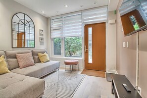 A modern living room with a sofa, ottoman, and a large window with blinds.