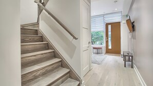 A modern interior with a wooden staircase leading to a room with a large window, a flat-screen TV mounted on the wall, and a small table. - Luxury Townhouse in Downtown Toronto (Toronto)