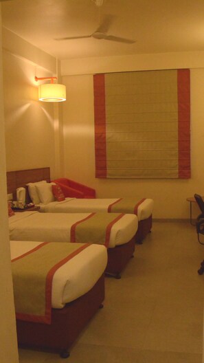 A hotel room with three single beds, a ceiling fan, a large window with blinds, and a bedside table with a lamp. - Max Hotel Jabalpur (Kolkata)