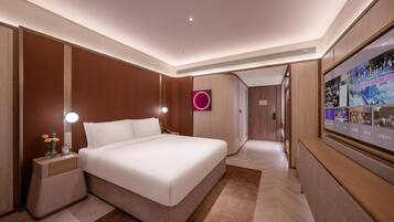 A modern hotel room with a large bed, bedside tables with lamps, a wall-mounted TV, and a wooden wardrobe.