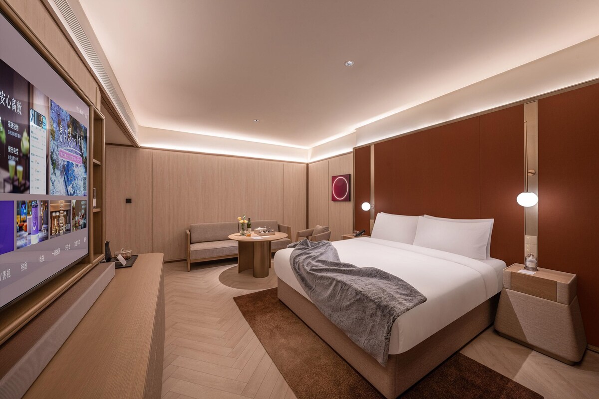 Une chambre d’hôtel moderne, dotée d’un grand lit, d’un canapé, d’une petite table et d’un téléviseur qui affiche un menu.