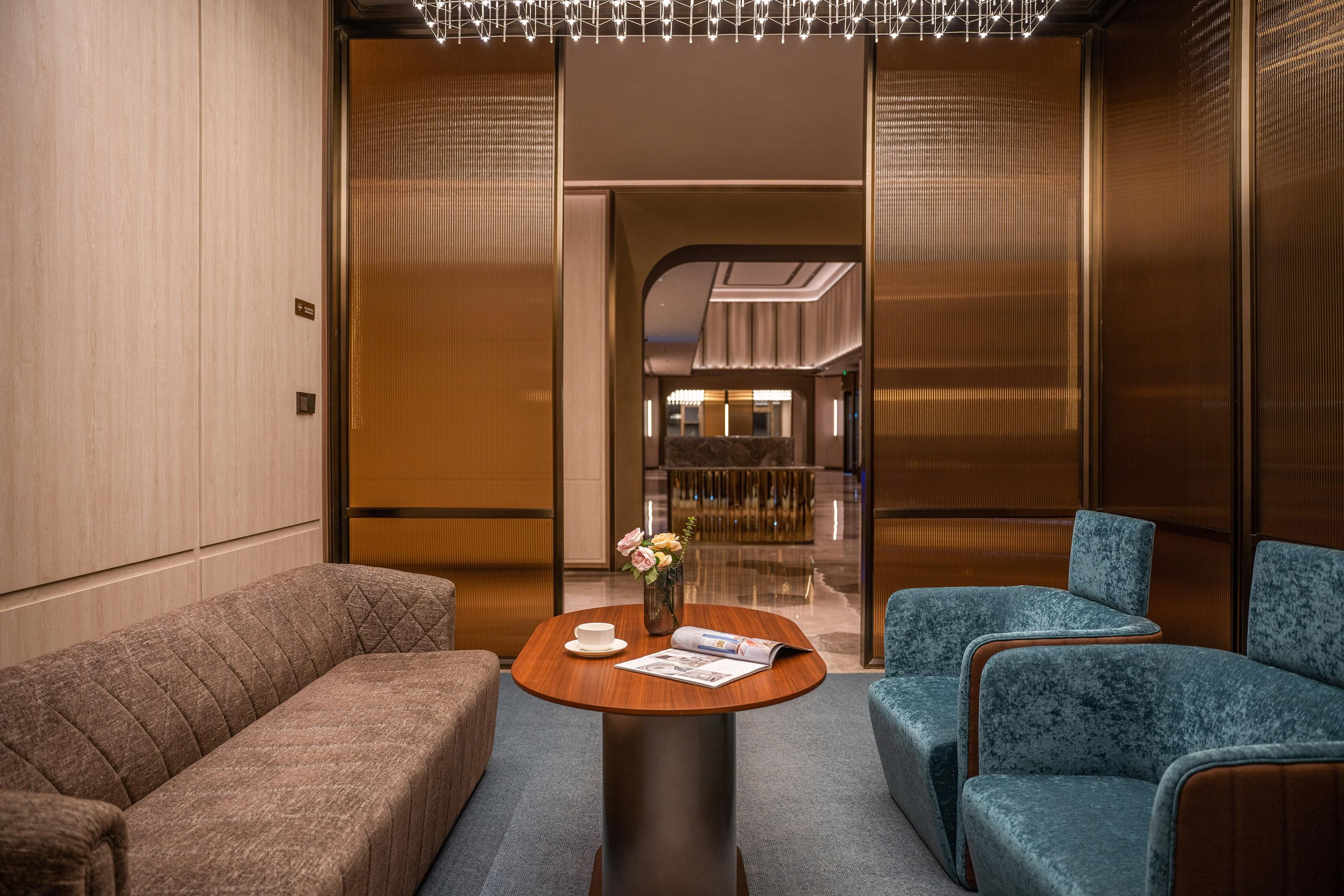 Un moderno vestíbulo de hotel con un mostrador de recepción de madera, dos sofás y un jarrón con flores.