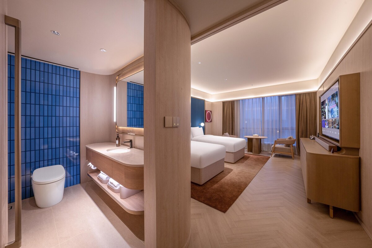 Une chambre d’hôtel moderne dotée d’un grand lit, d’un canapé séparé, d’une télévision et d’une salle de bain avec un mur recouvert de carreaux bleus.