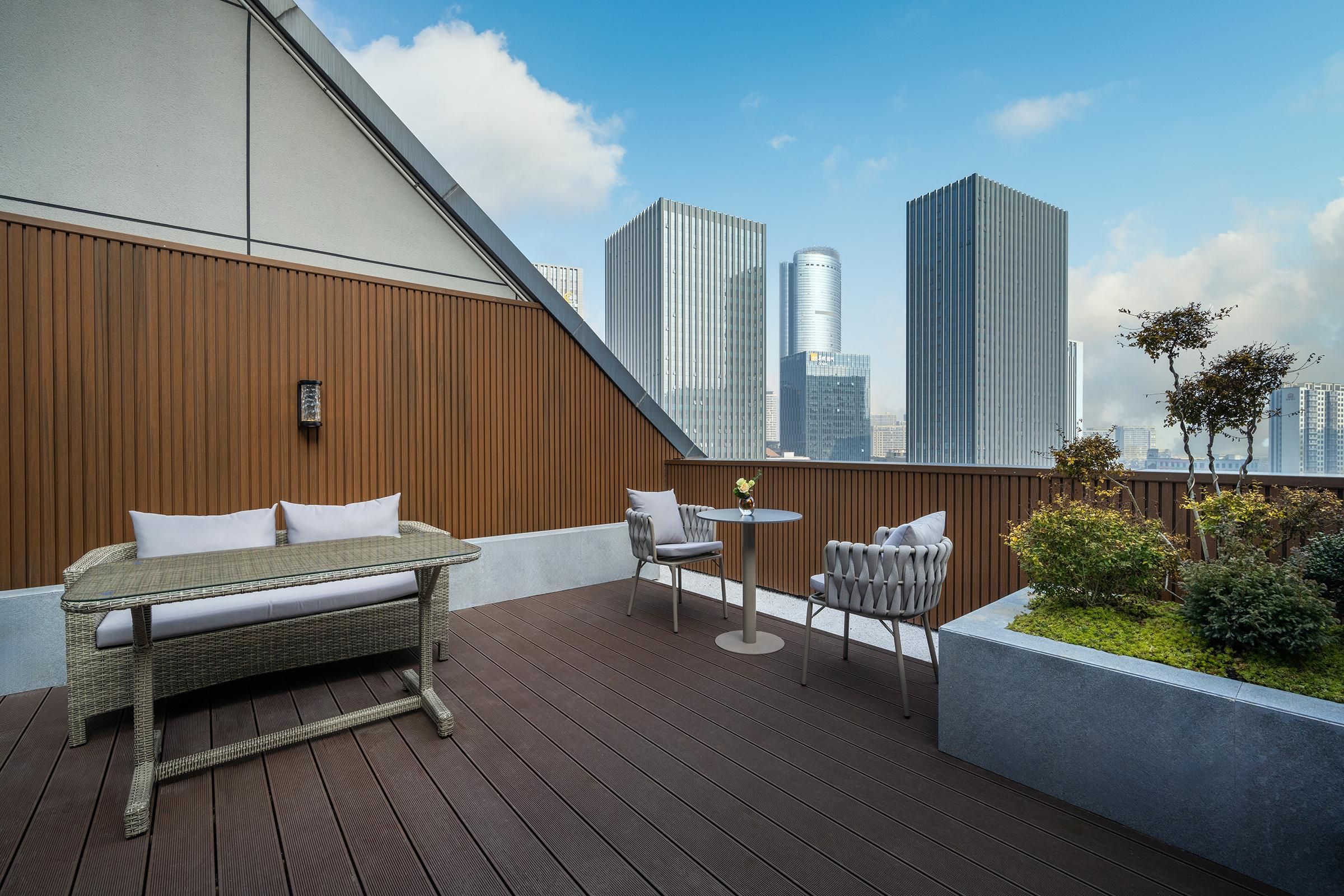 En tagterrasse med træterrasse, en fletsofa, to stole, et lille bord og en plantekasse med grønt.