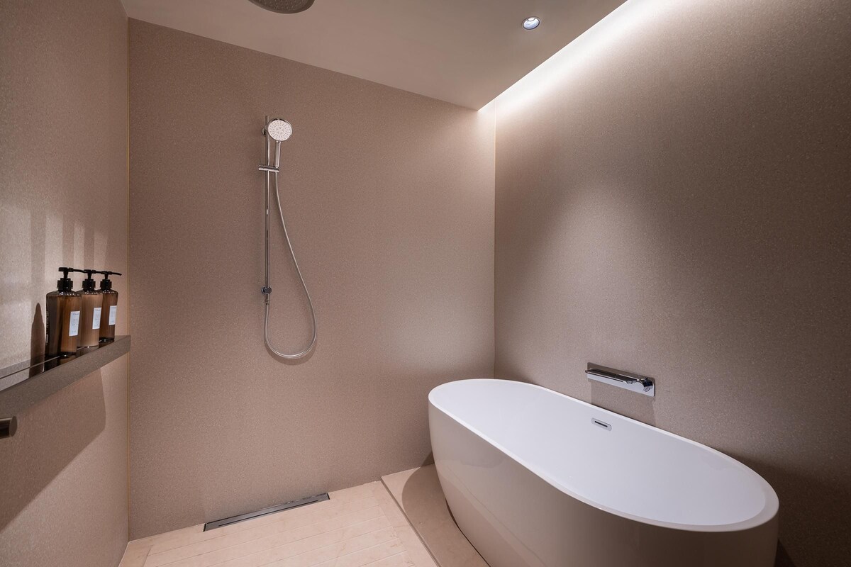 Une salle de bain moderne avec une baignoire sur pieds, une pomme de douche et une étagère contenant des articles de toilette.