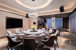 Una sala de conferencias moderna con una mesa redonda, varias sillas, un televisor de pantalla plana grande y un elegante aplique de techo.