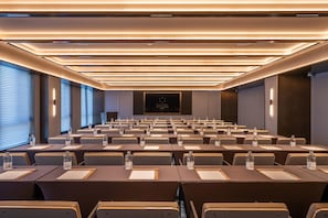 Sala de conferências com fileiras de mesas e cadeiras, equipada com placas de identificação e garrafas de água.