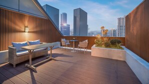 A rooftop terrace with a wicker sofa, two round tables, and chairs, overlooking a cityscape with tall buildings. - Crystal Orange Hotel Nanjing Southeast University (Nanjing)