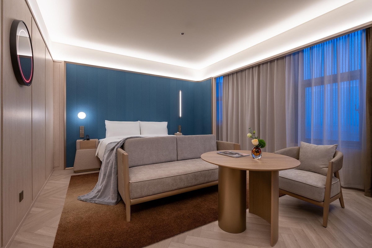 Une chambre d’hôtel moderne avec un canapé, une table basse ronde et un lit doté d’une table de chevet.