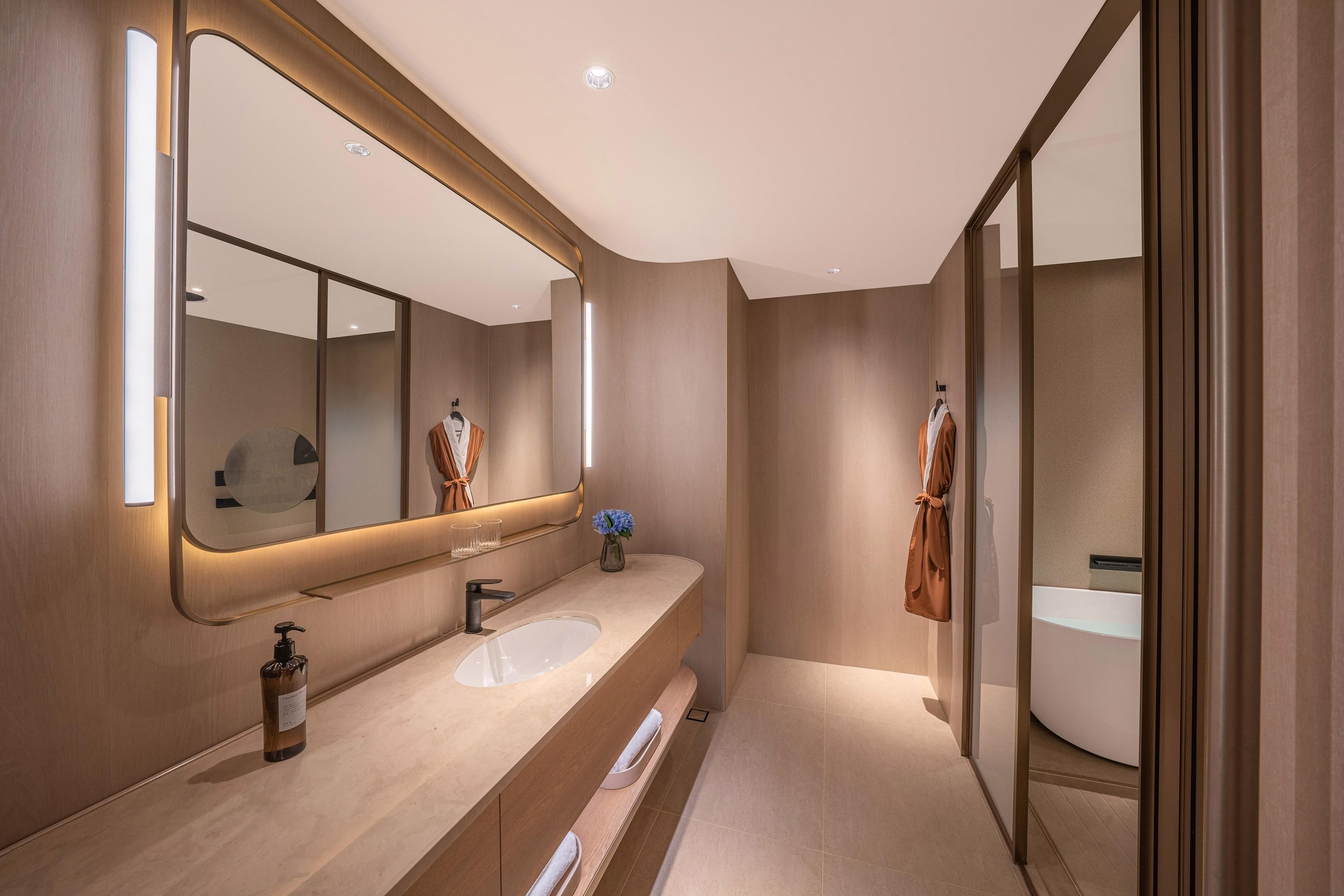 Un baño moderno con un espejo grande, un lavamanos y una bañera.