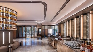 A modern bar area with a curved shelving unit displaying bottles, a bar counter with glasses, and a seating area with a sofa and small tables. - Crystal Orange Hotel Nanjing Southeast University (Nanjing)