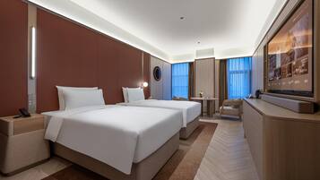 Habitación de hotel con dos camas, un escritorio, un televisor y un ventanal con cortinas.