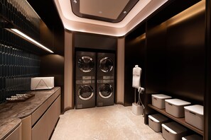 Une buanderie moderne équipée de deux machines à laver fixées au mur, d’un plan de travail avec un distributeur de serviettes et de bacs de rangement bien organisés.