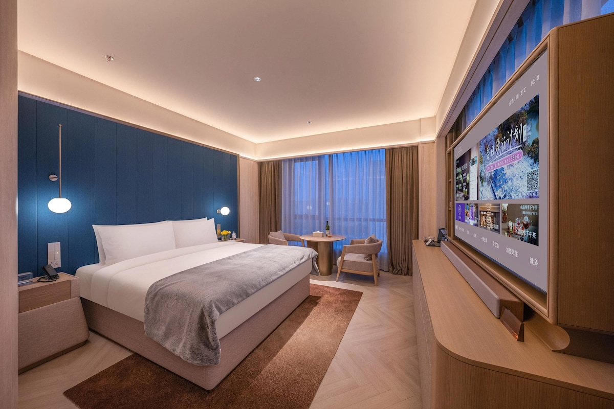 Une chambre d’hôtel moderne dotée d’un grand lit, de tables de chevet, d’une télévision et d’un coin salon avec une table et des chaises.