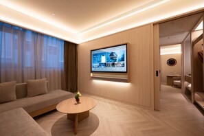 Una habitación de hotel moderna con un televisor de pantalla plana grande montado en la pared, un sofá, una mesa de centro redonda y suelo de madera.