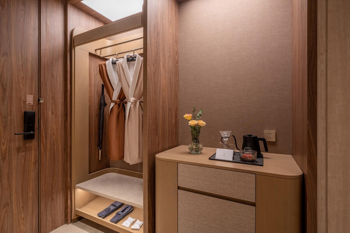 Une salle de bain moderne et compacte, dotée d’un meuble-lavabo en bois, d’une zone douche et d’une petite table où sont rangés les articles de toilette.